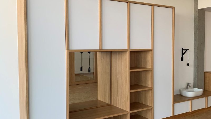 Une grande armoire en bois avec des portes blanches et des étagères dans une pièce.